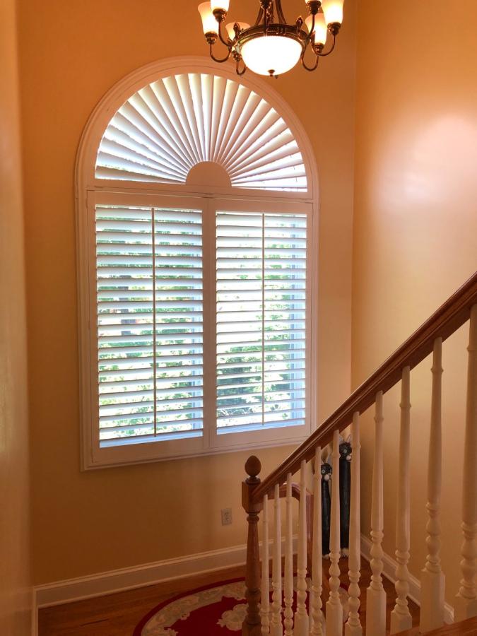 Carolina Blinds installation — sunburst arch shutter with plantation shutters in two-story stairwell